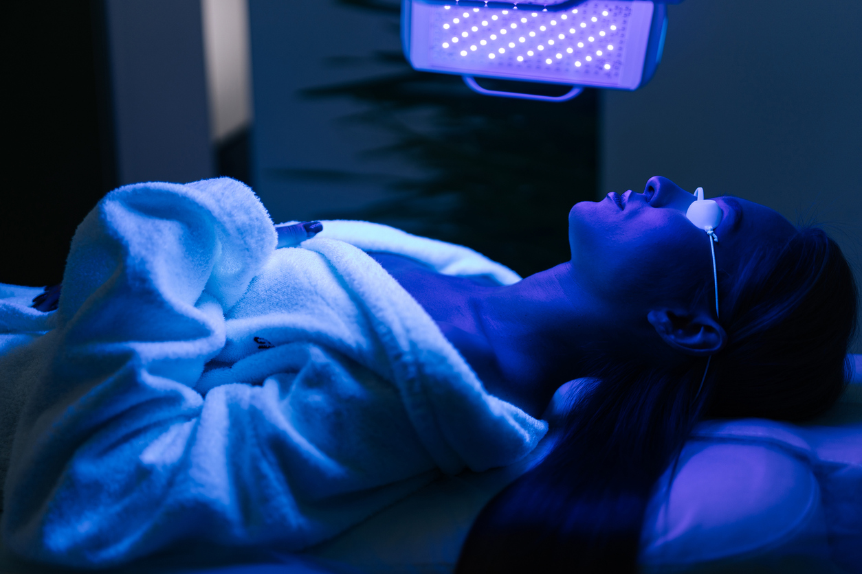 Young woman in glasses having blue LED light facial photodynamic therapy treatment in beauty salon. Female client having non invasive type of phototherapy.